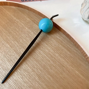 Detailed macro view of a minimalist black hair pin featuring a glossy blue sphere on wood