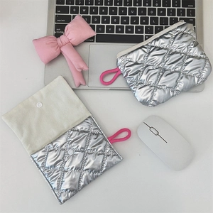 Detail of silver quilted makeup pouches with zipper and snap flap closure on a desk