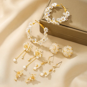 Detail of 18K gold earrings set featuring zircon, pearls and floral designs on beige fabric