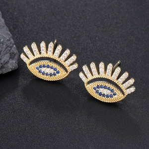 Golden evil eye stud earrings with blue and clear zircon crystals on dark stone backdrop