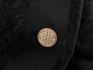 Détail d'un bouton doré en relief sur le tissu en tweed noir d'une robe élégante