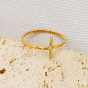 Polished gold stainless steel cross ring for women on white silk and stone backdrop