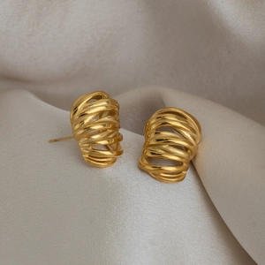 Detail shot of golden multi-layer spiral C-shape earrings on champagne silk background