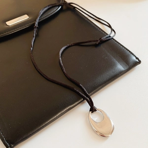 Detailed close-up of a silver teardrop pendant necklace on black leather texture