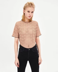 Dettaglio del pizzo floreale con bordo nero ondulato sul top beige elegante da donna