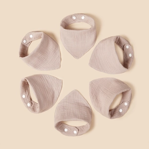 Detailed texture of six beige cotton muslin baby bibs with adjustable snap closures