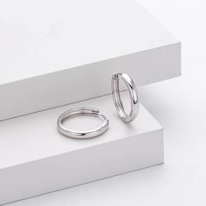 Polished silver hoop earrings displayed on white geometric platforms with modern lighting