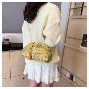 Elegant yellow embroidered evening bag with tassel and gold chain strap shown on model.