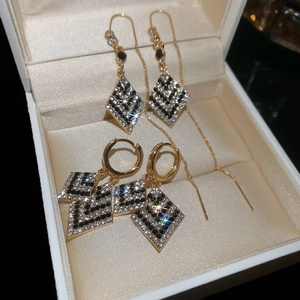 Détail de boucles d'oreilles losange à pompons et créoles dans un coffret