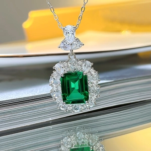 Macro detail of silver necklace featuring square emerald pendant with crystal halo