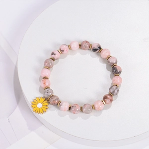 Macro shot of pink zebra stone beaded bracelet with gold spacers and yellow daisy charm