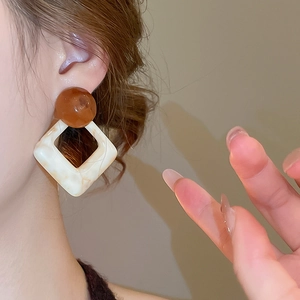 Close-up of geometric resin drop earrings with amber beads and white marble square patterns
