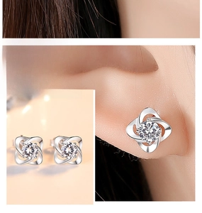 Detailed view of silver clover stud earrings with cubic zirconia and on-ear wear display