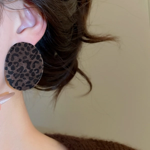 Close-up of leopard print flocked oval stud earrings worn by a model in warm light
