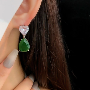 Détail de boucles d'oreilles en perles avec pierres vertes et cœurs portées par un modèle