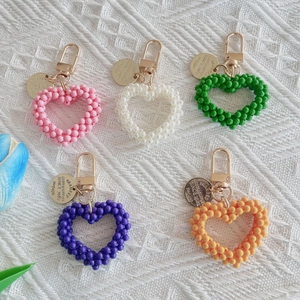 Five colorful handmade beaded heart keychains with gold metal clasps on white fabric