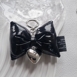 Detail of black bow keychain with silver heart charm and metal ring on white surface