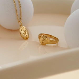 Minimalist gold rose embossed pendant necklace and matching flower ring on warm background