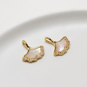 Macro shot of two golden ginkgo leaf pendants with white shell inlay and zircons