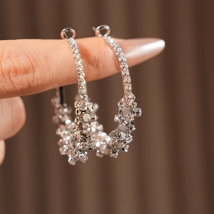 Gros plan de grandes créoles argentées avec strass brillants tenues par une main
