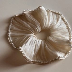 Macro view of cream silk scrunchie with detailed pearl trim edging and pleated texture