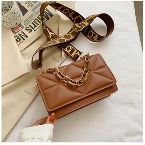 Detail of brown quilted crossbody bag with wide jacquard strap and chain accessory