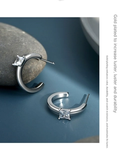 Macro detail of silver C-shape earrings with square zircon on a minimalist blue background