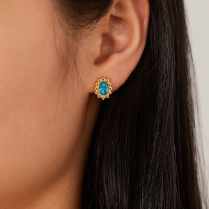 Detail of vintage gold-plated stud earring with oval blue gemstone on a model's ear