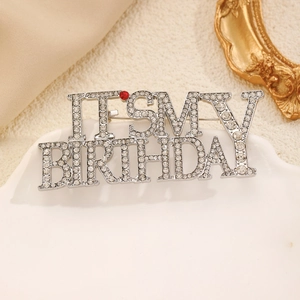 Detail of silver rhinestone brooch with Its My Birthday lettering on white ceramic plate