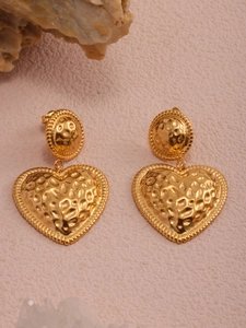 Detailed macro of gold heart earrings with hammered texture on a textured pink surface