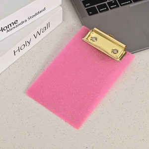 Close-up of pink glitter acrylic clipboard with a golden metal clip on a modern desk
