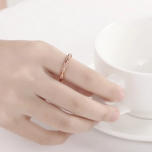 Close-up of minimalist rose gold bamboo joint open ring worn by model holding white cup