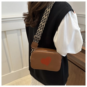 Detail of brown litchi pattern bag with red heart and geometric woven strap