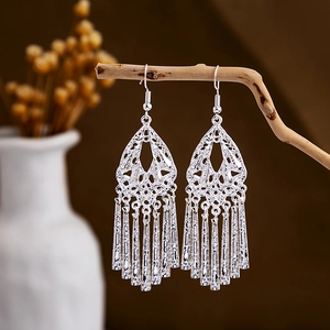 Macro detail of silver-tone hollow peacock tassel earrings hanging on a rustic branch