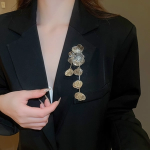 Detail of gold floral brooch with hollow petals and long tassel on a black blazer
