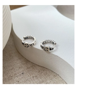Detailed macro view of vintage silver smiley face hoop earrings on a textured stone surface