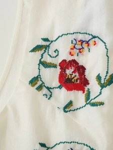 Détail de la broderie florale avec fleurs rouges sur tissu de gilet en coton beige
