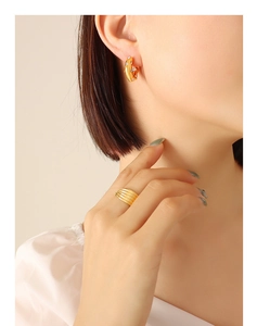 Detail of gold C-shaped earrings with zircons and textured layered ring on model