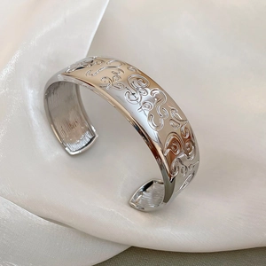 Close-up of silver oval bangle with intricate floral engravings on silky background