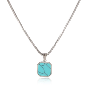 Macro detail of silver box chain with an octagonal turquoise pendant on white surface