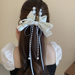 Detail of elegant white fabric bow hair claw with long pearl tassels and blue trim details
