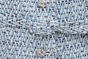 Detailed macro view of tweed vest fabric with silver woven metal button and texture