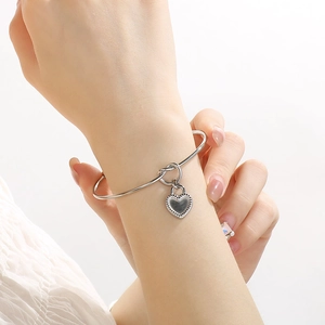 Close-up of a silver stainless steel knot bangle with a heart lock pendant on a wrist