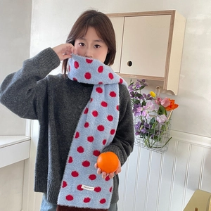 Close-up of plush blue and red polka dot scarf worn by model in a cozy indoor setting