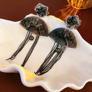 Detail of black fan-shaped earrings with 3D roses and long tassels in a shell tray