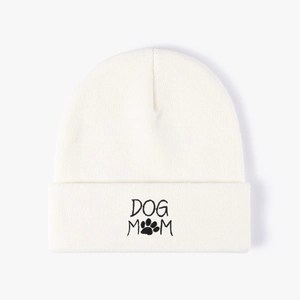 White knit beanie with black Dog Mom embroidery and paw print on a clean white background