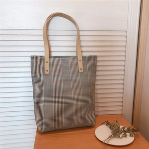 Detail of vintage plaid canvas tote bag with brown leather handles and rivet accents