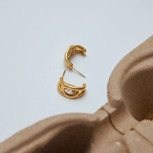 Detail of twisted double-layer gold earrings with a sparkling zircon inlay for women