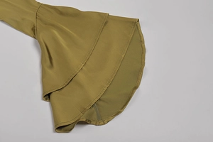 Dettaglio di un abito verde oliva con eleganti polsini a campana a doppio strato e seta