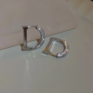 Macro shot of silver letter D earrings with sparkling zircon pave setting on grey surface